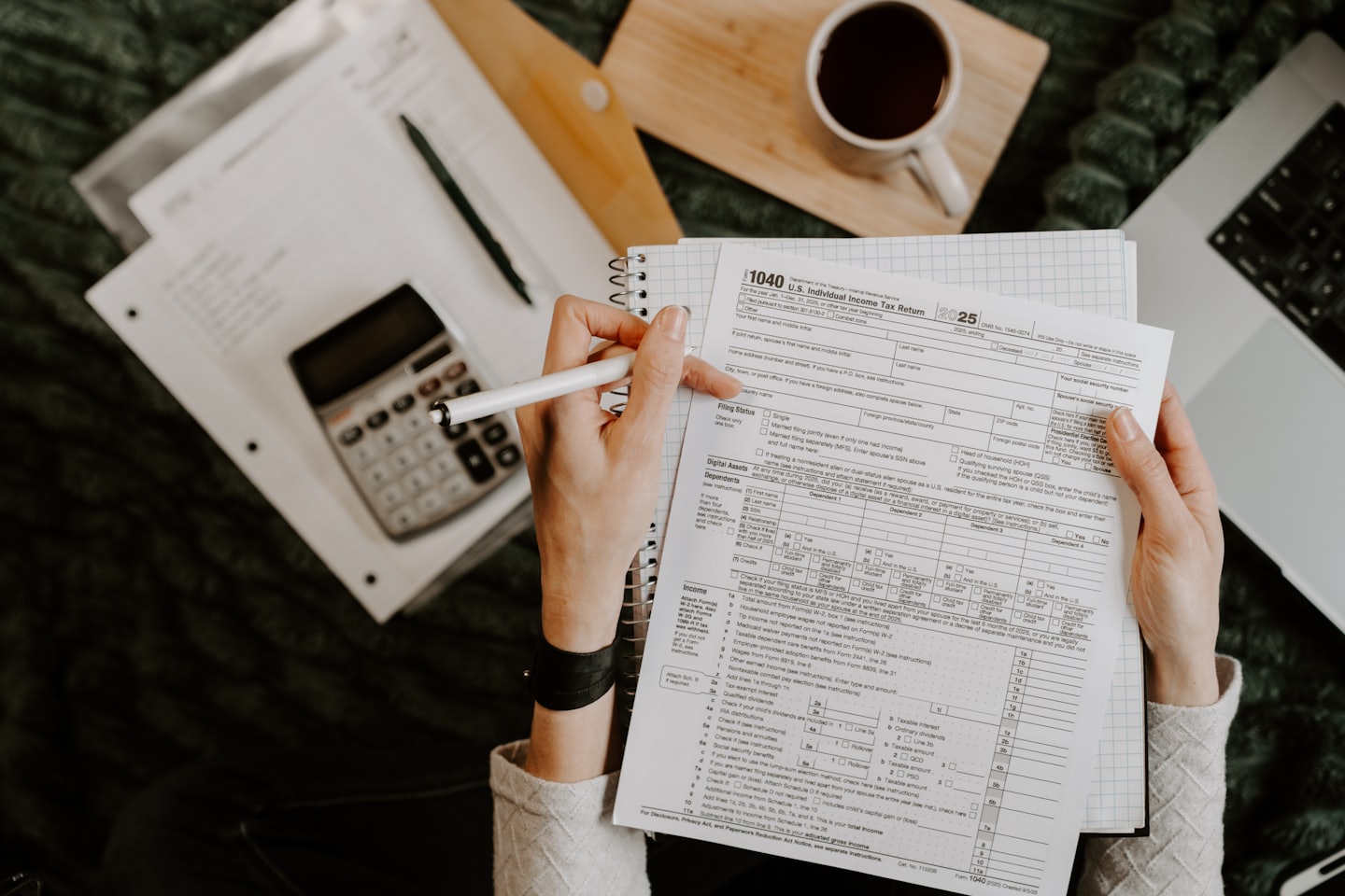 Hands reviewing a tax form with a pen, laptop, and calculator.